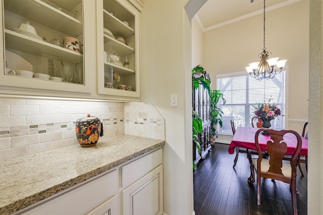 23615 Dolci Ln, Richmond, TX 77406 - kitchen featuring ornamental molding, light stone counters, a chandelier, glass insert cabinets, and decorative backsplash