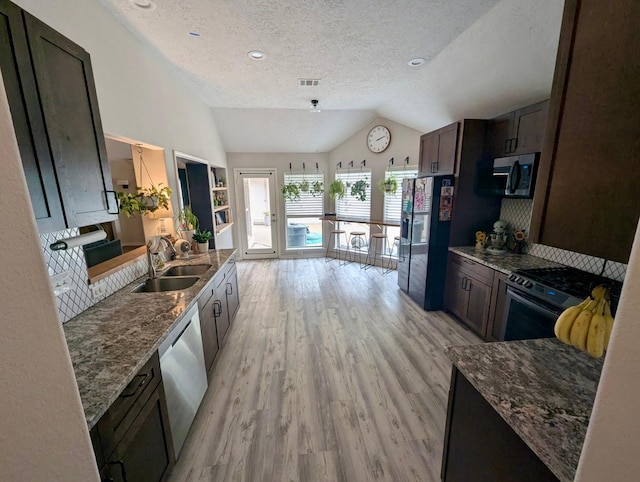 kitchen with appliances with stainless steel finishes, a sink, lofted ceiling, a textured ceiling, and light wood-style flooring