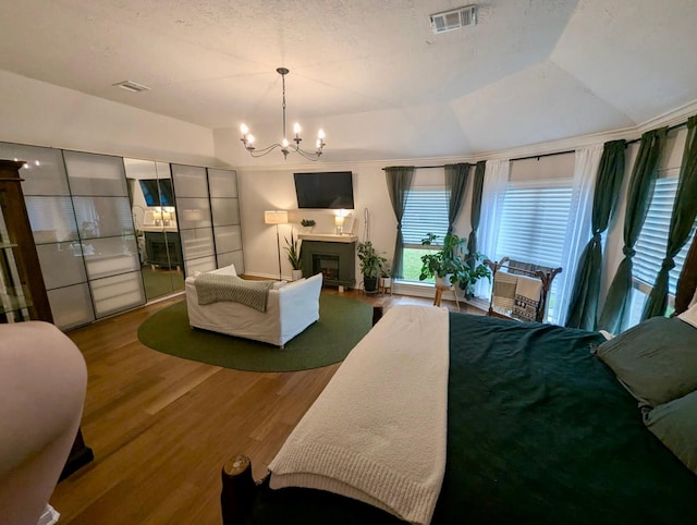 bedroom with wood finished floors, a chandelier, a fireplace, and lofted ceiling