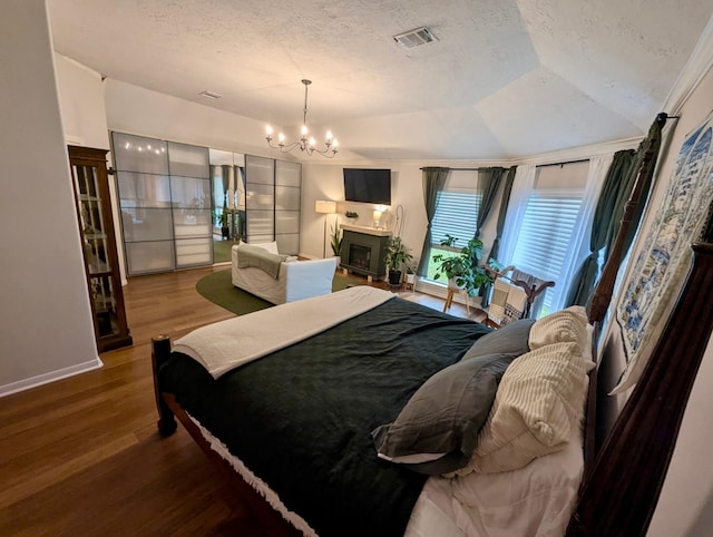 bedroom with a textured ceiling, wood finished floors, a chandelier, baseboards, and a fireplace