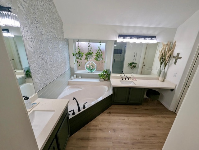 full bathroom featuring a garden tub, wood finished floors, wallpapered walls, and two vanities