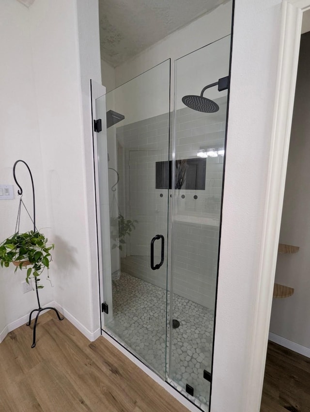 bathroom featuring wood finished floors, baseboards, and a shower stall