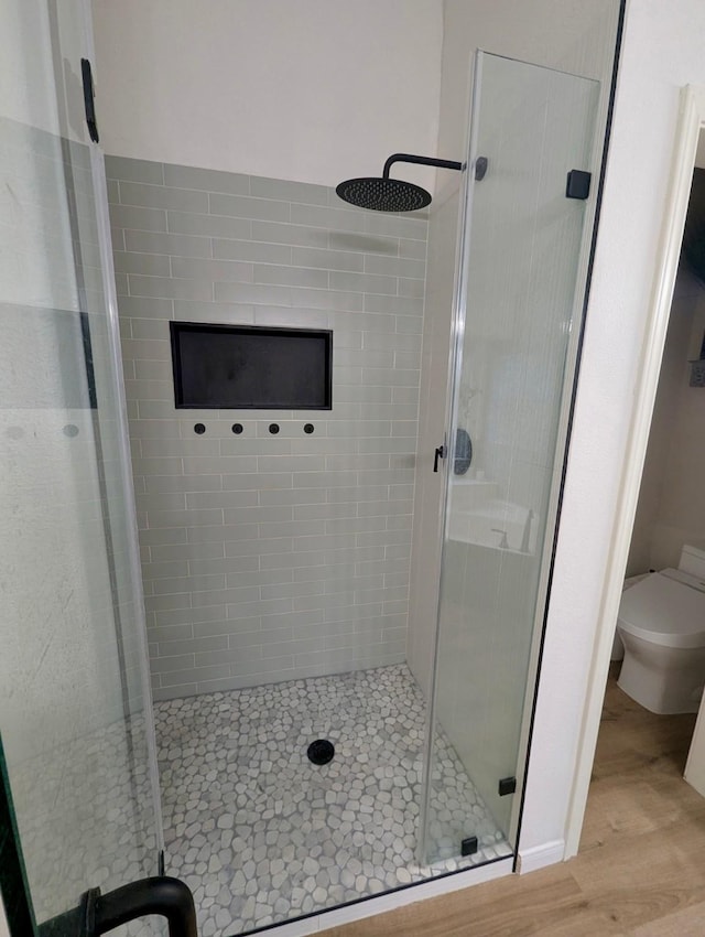 full bathroom with a stall shower, toilet, and wood finished floors