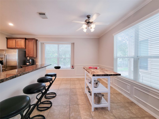 1241 Prince St, Houston, TX 77008 - kitchen with stainless steel fridge, ornamental molding, ceiling fan, dark stone countertops, and brown cabinetry