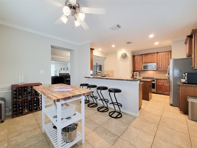 1241 Prince St, Houston, TX 77008 - kitchen featuring appliances with stainless steel finishes, ceiling fan, ornamental molding, dark stone counters, and brown cabinets