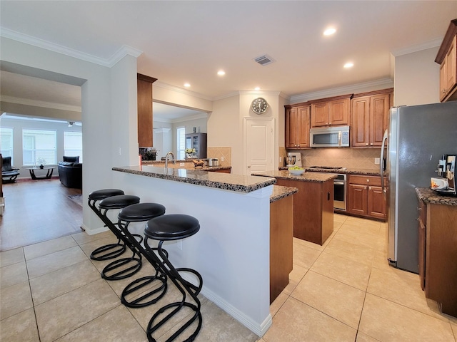1241 Prince St, Houston, TX 77008 - kitchen with appliances with stainless steel finishes, light tile patterned floors, a breakfast bar area, dark stone counters, and crown molding