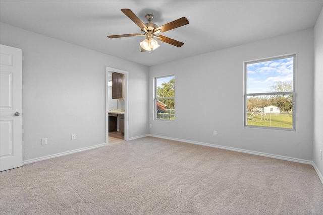 unfurnished bedroom with light carpet, baseboards, ensuite bath, and a ceiling fan
