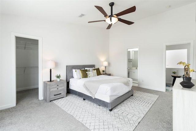bedroom with light colored carpet, a walk in closet, a closet, ensuite bathroom, and vaulted ceiling