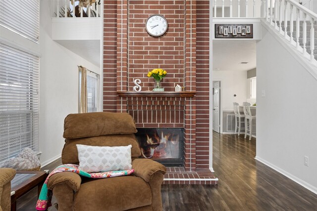 sitting room featuring a towering ceiling, wood finished floors, baseboards, stairs, and a brick fireplace
