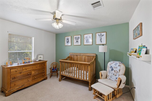 carpeted bedroom featuring a nursery area, ceiling fan, and baseboards