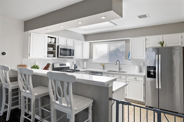 kitchen featuring stainless steel appliances, a sink, a kitchen bar, light countertops, and backsplash