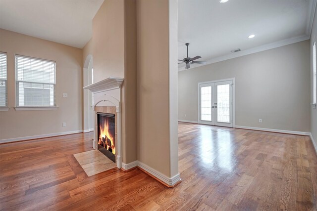 unfurnished living room with a ceiling fan, wood finished floors, a tiled fireplace, baseboards, and crown molding