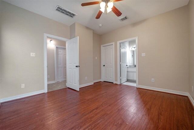 unfurnished bedroom featuring wood finished floors, baseboards, ensuite bathroom, and a ceiling fan