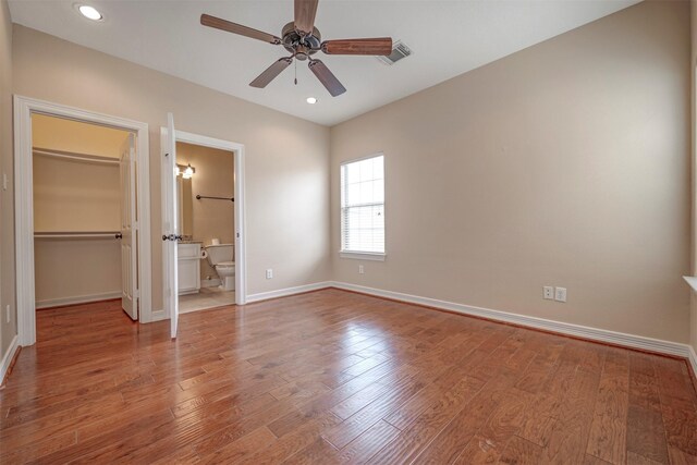 unfurnished bedroom featuring a walk in closet, baseboards, a closet, wood finished floors, and ensuite bathroom