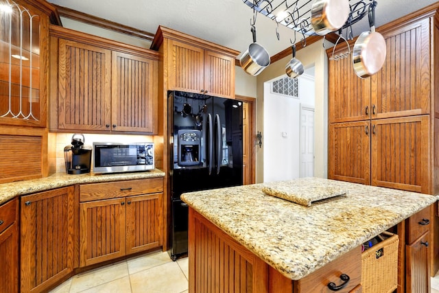 4010 Haven Pines Dr, Houston, TX 77345 - kitchen featuring black refrigerator with ice dispenser, stainless steel microwave, brown cabinetry, light stone counters, and crown molding