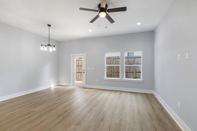 spare room with a chandelier, light wood-style flooring, a ceiling fan, baseboards, and recessed lighting