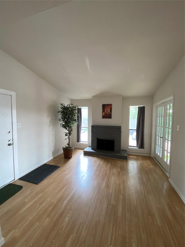 unfurnished living room with a brick fireplace, wood finished floors, baseboards, and lofted ceiling