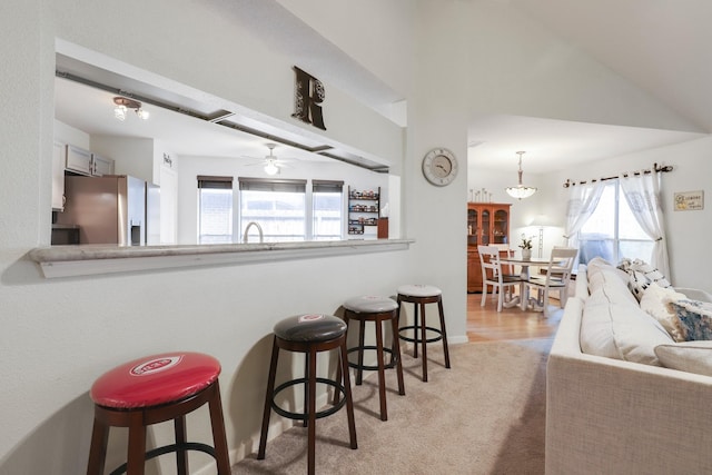 kitchen with stainless steel fridge with ice dispenser, a breakfast bar, light colored carpet, a peninsula, and ceiling fan