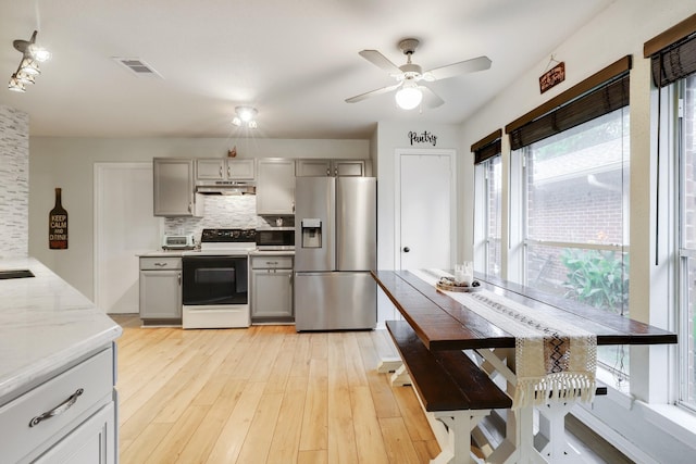 kitchen featuring stainless steel appliances, under cabinet range hood, gray cabinets, decorative backsplash, and a ceiling fan