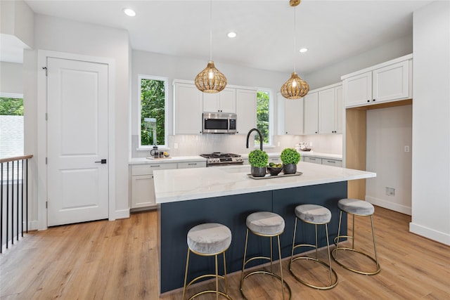 514 Janisch Rd, Houston, TX 77018 - kitchen featuring appliances with stainless steel finishes, white cabinetry, light wood finished floors, an island with sink, and baseboards