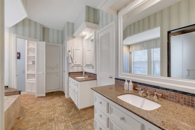 bathroom featuring backsplash, wallpapered walls, and two vanities