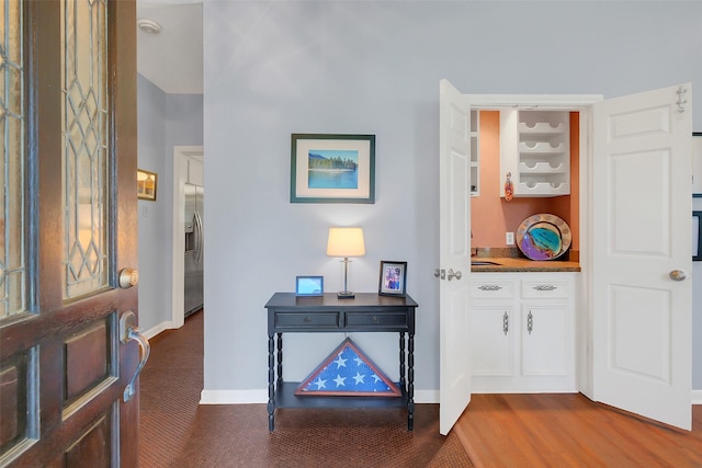 foyer entrance with baseboards and dark carpet