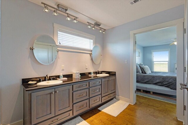bathroom featuring ensuite bath, wood finished floors, double vanity, ceiling fan, and baseboards