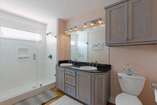 full bathroom featuring a shower stall, toilet, double vanity, a textured ceiling, and wood finished floors