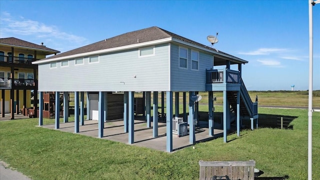 rear view of house featuring a patio, a yard, and roof with shingles