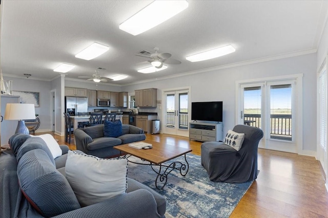 living room featuring ornamental molding, light wood finished floors, a ceiling fan, and baseboards