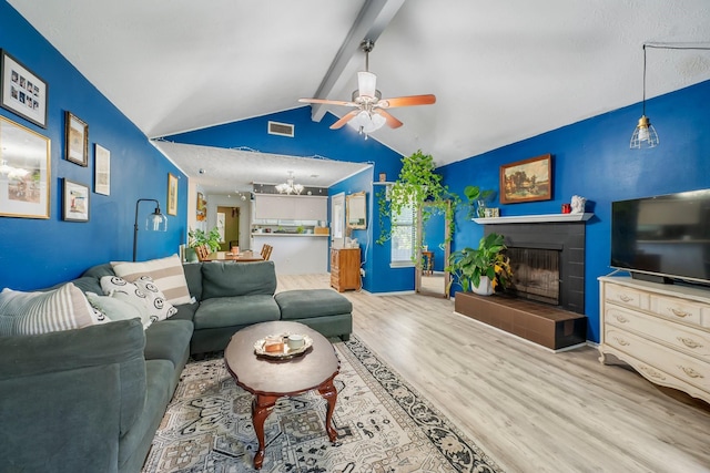 living room featuring a ceiling fan, a chandelier, wood finished floors, and a fireplace with raised hearth