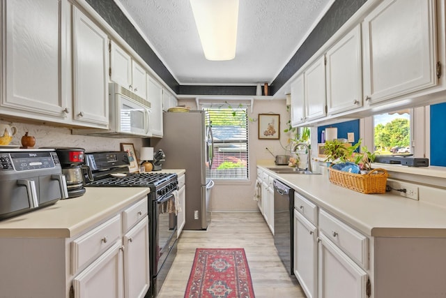 kitchen with black appliances, a sink, light wood-type flooring, and light countertops