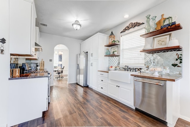 81 San Simeon Dr, Manvel, TX 77578 - kitchen with stainless steel appliances, open shelves, a sink, arched walkways, and wall chimney exhaust hood