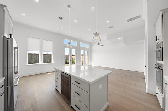 kitchen featuring appliances with stainless steel finishes, wine cooler, light wood-style flooring, a kitchen island, and baseboards