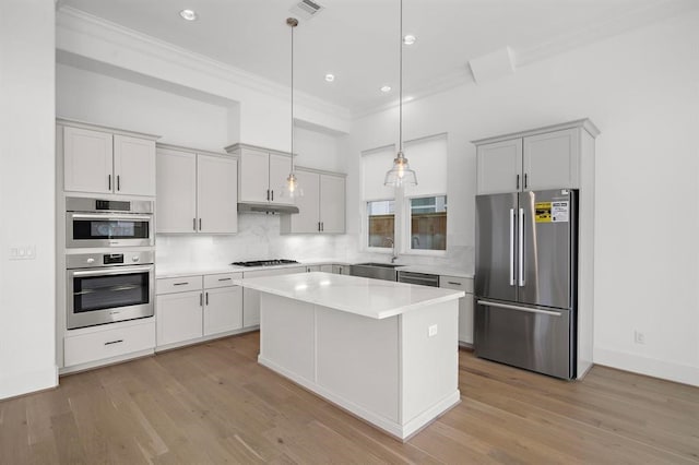 kitchen featuring appliances with stainless steel finishes, ornamental molding, a kitchen island, a sink, and decorative backsplash