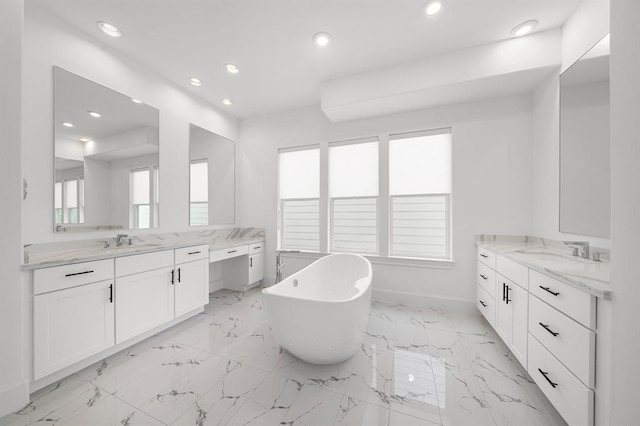 bathroom featuring recessed lighting, a freestanding tub, two vanities, baseboards, and marble finish floors