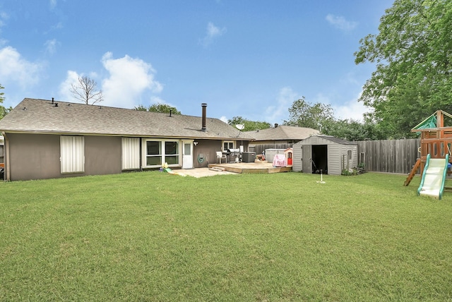 back of house with a storage shed, a playground, an outdoor structure, a shingled roof, and a wooden deck