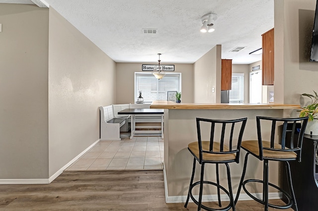 kitchen with a breakfast bar, light wood finished floors, baseboards, a textured ceiling, and a peninsula
