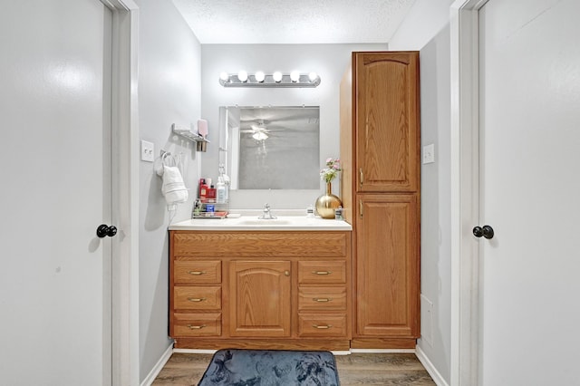 bathroom with wood finished floors, vanity, a textured ceiling, ceiling fan, and baseboards