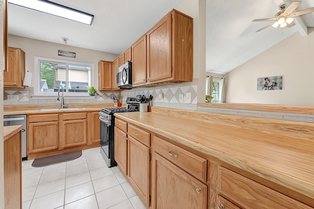 kitchen featuring stainless steel appliances, a sink, tasteful backsplash, light tile patterned flooring, and lofted ceiling