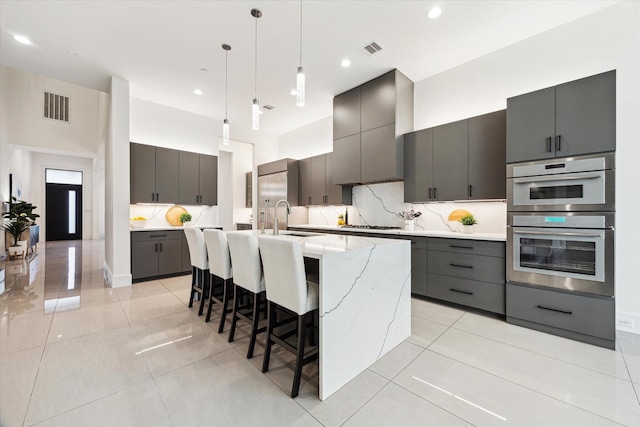 kitchen with a sink, decorative backsplash, hanging light fixtures, an island with sink, and gray cabinets