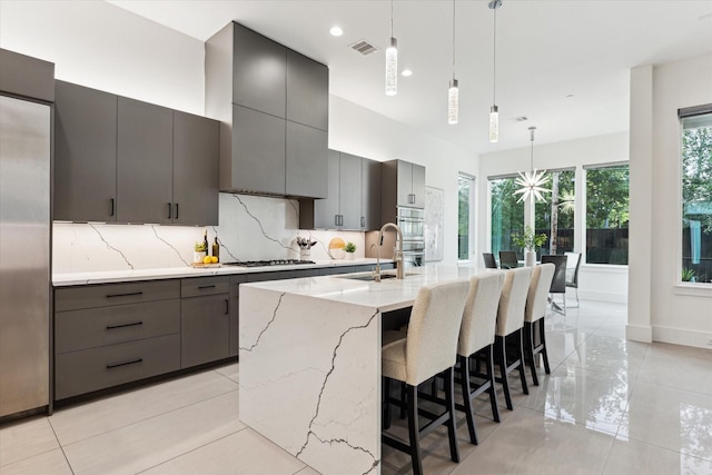 kitchen with gas cooktop, decorative backsplash, a kitchen island with sink, pendant lighting, and gray cabinetry