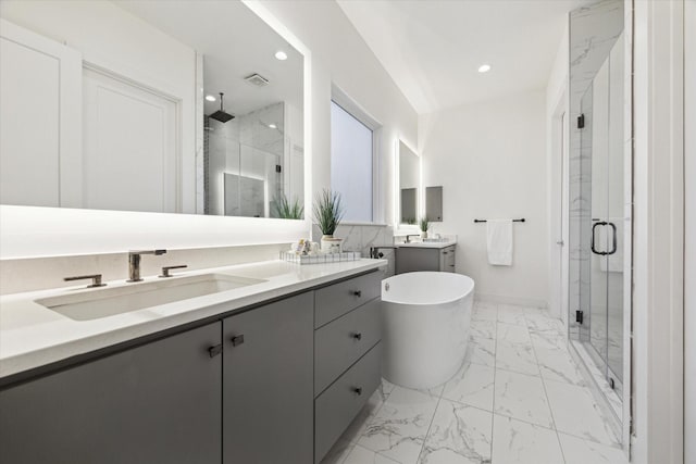 bathroom featuring marble look tile flooring, a shower stall, recessed lighting, two vanities, and a freestanding tub
