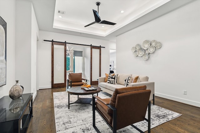living room with a barn door, dark wood-style floors, a raised ceiling, baseboards, and recessed lighting