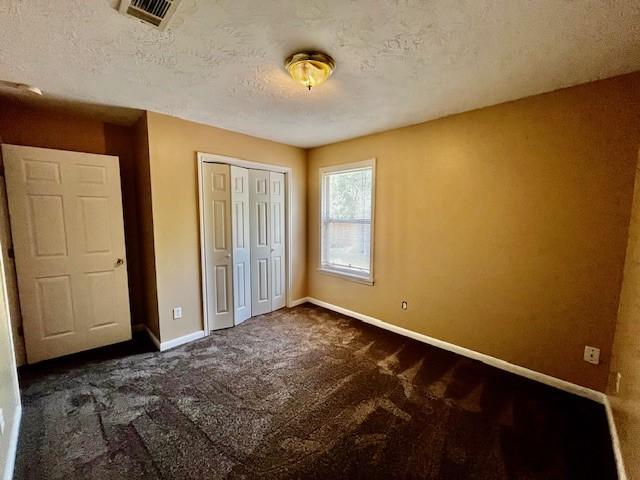 10826 Buffum St, Houston, TX 77051 - unfurnished bedroom featuring dark colored carpet, baseboards, a closet, and a textured ceiling