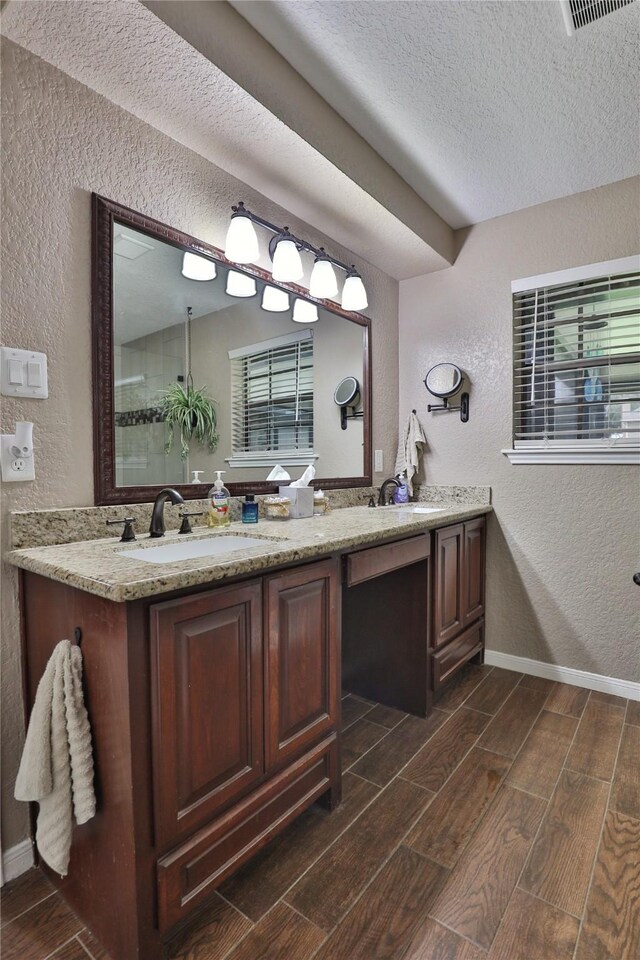 bathroom featuring a textured wall, wood tiled floors, double vanity, a textured ceiling, and healthy amount of natural light