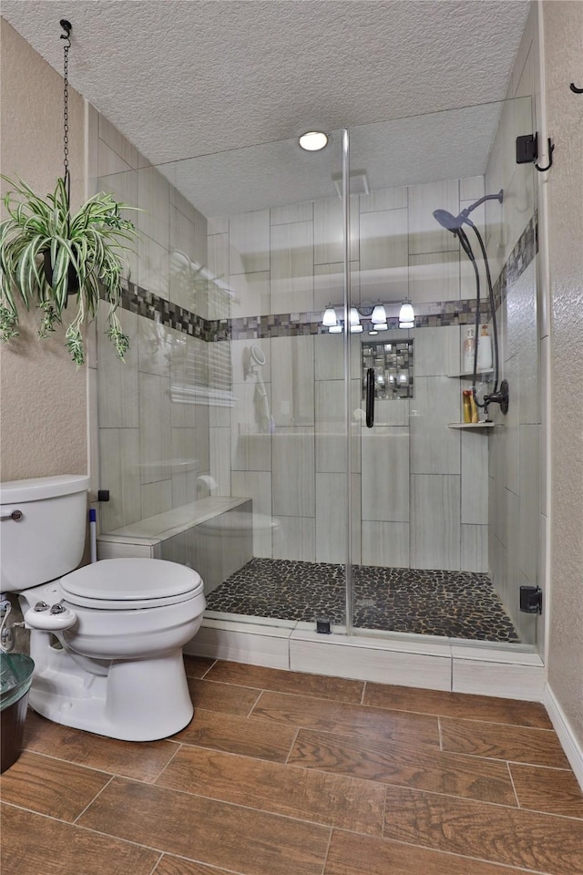 full bath featuring toilet, wood tiled floors, a textured ceiling, and a stall shower