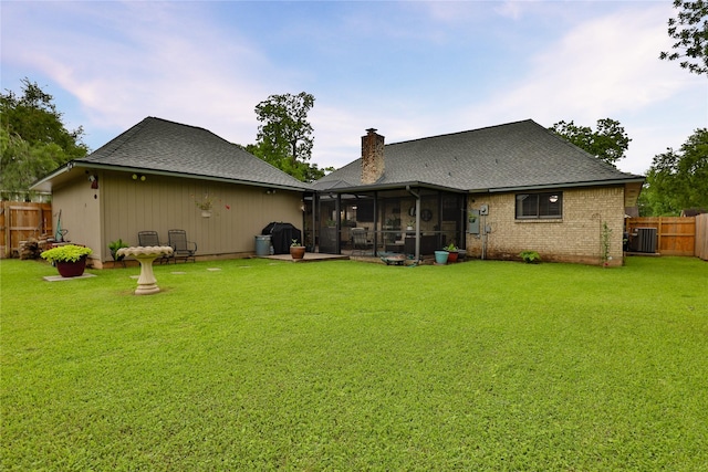 rear view of property with a sunroom, a chimney, a shingled roof, and cooling unit