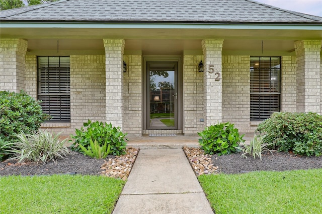 property entrance with a shingled roof, brick siding, and a porch
