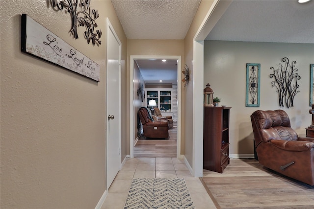 corridor featuring a textured ceiling, light tile patterned flooring, and baseboards